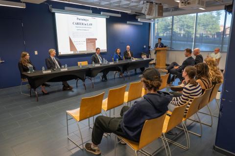 Legal professionals participate in Westfield State University's Pursuing a Career in Law forum as students listen from the audience and a moderator stands at the podium