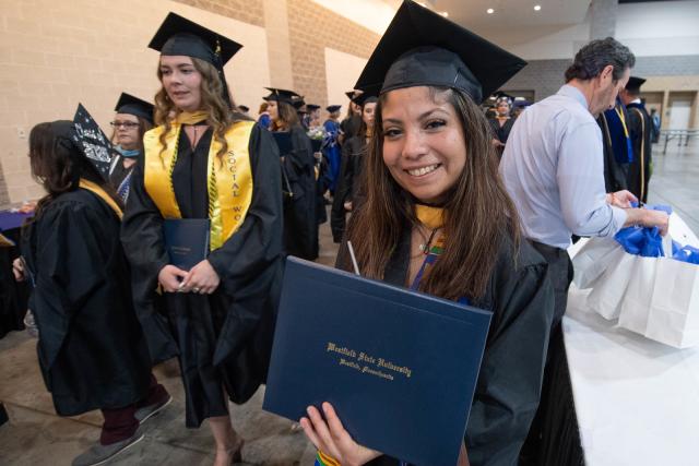 MSW student at commencement proudly smiling with diploma.