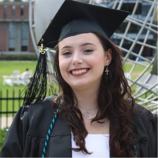 Art alum Christina smiling in cap and gown in front of the campus globe.